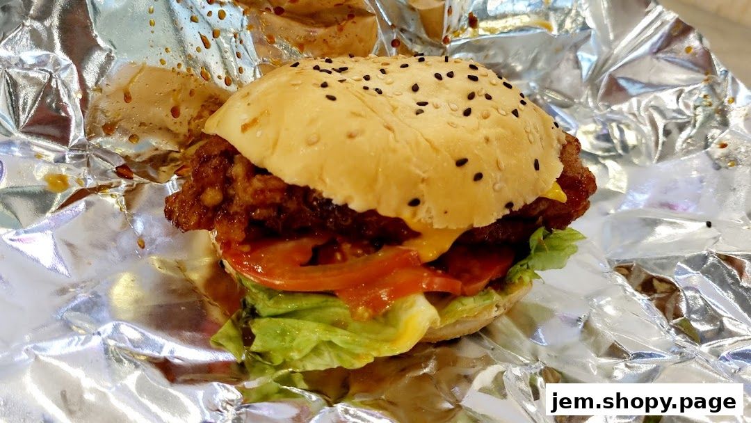 A close-up of a crispy chicken burger with lettuce, tomato, and cheese, wrapped in foil.