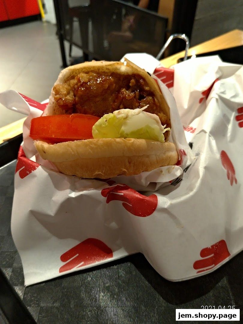 A close-up of a crispy chicken burger with tomato and lettuce on a tray.