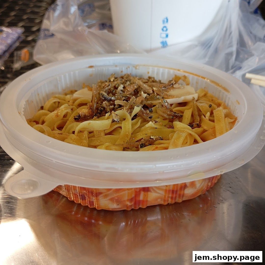 A close-up of a takeaway noodle dish with anchovies and sauce.