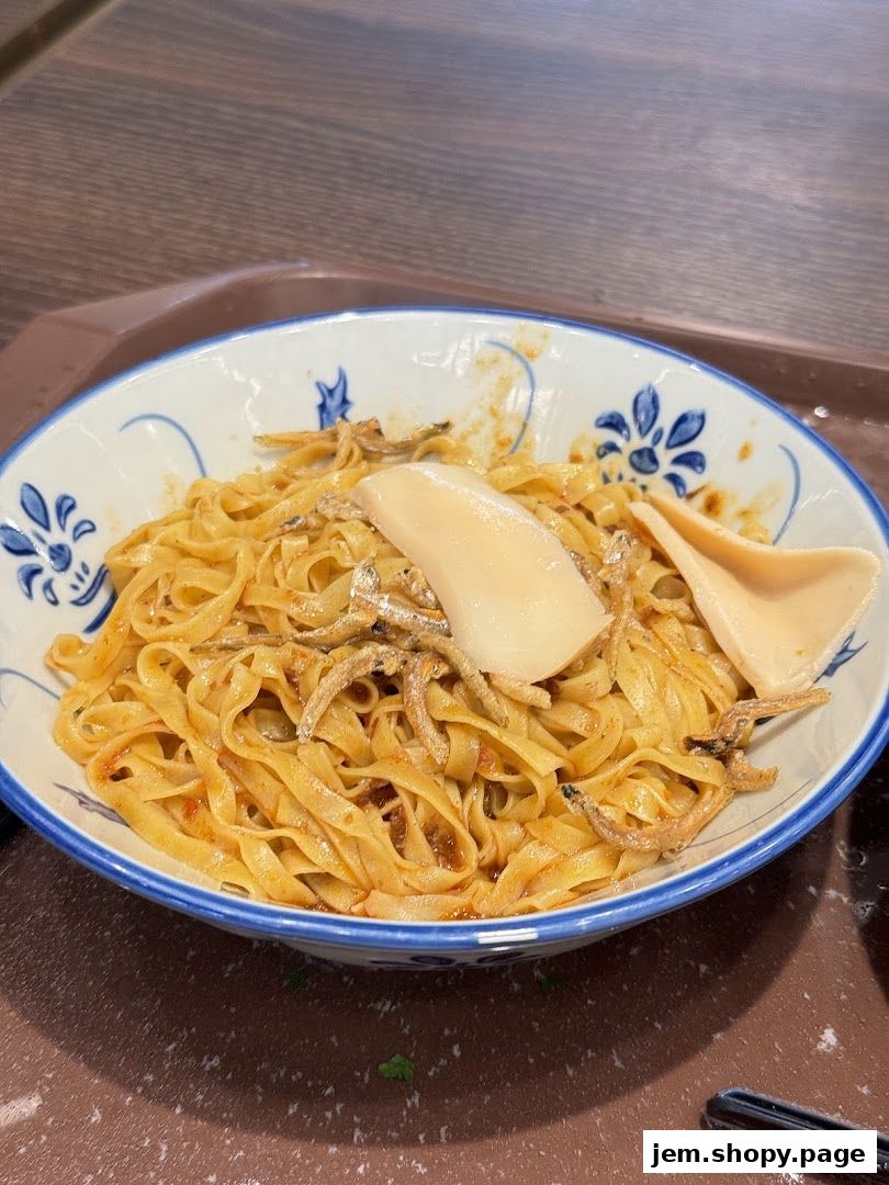 A close-up of a bowl of noodles with dried anchovies and slices of fish cake.