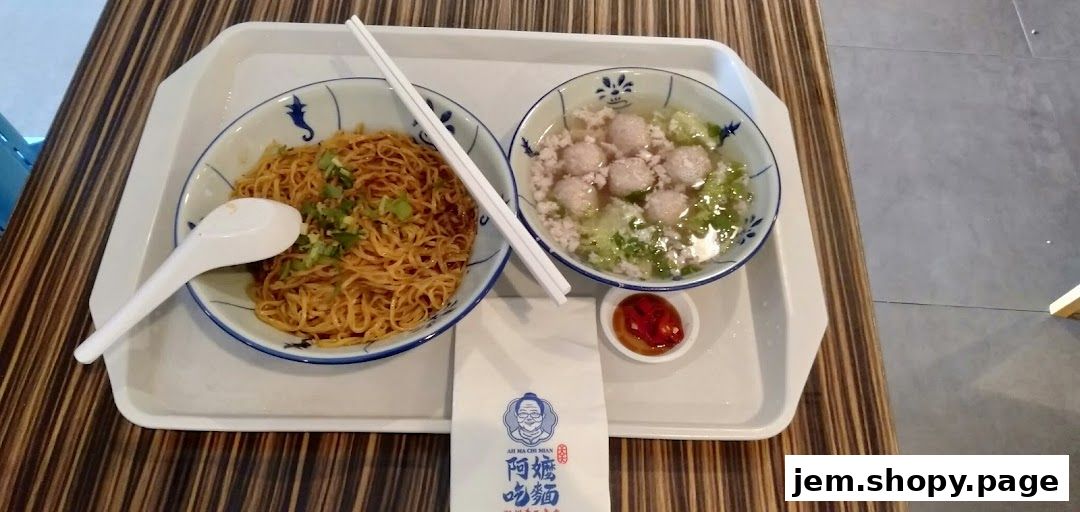 A bowl of dry noodles and a bowl of soup with meatballs served on a tray.