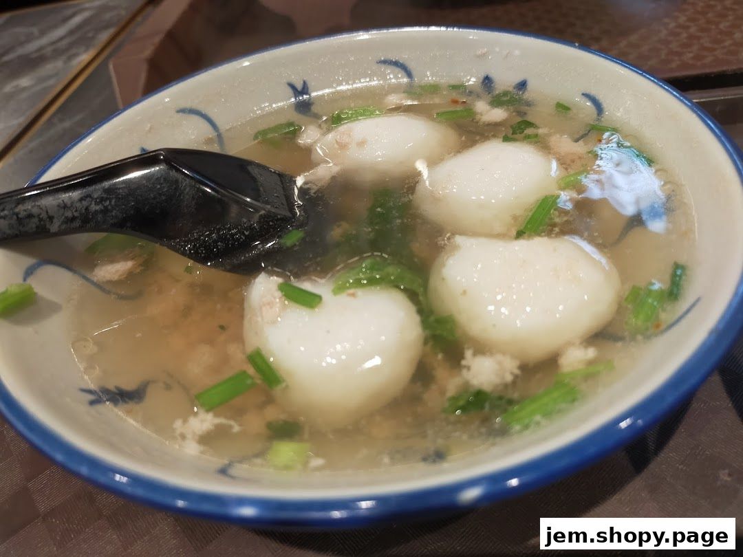 A close-up of a bowl of soup with fish balls and minced meat, garnished with spring onions.