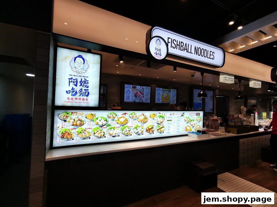 A food stall named Ah Ma Chi Mian, specializing in fishball noodles, with a large illuminated menu.
