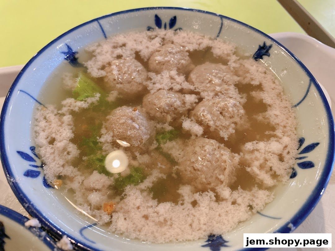 A close-up of a bowl of soup with meatballs and greens, topped with foam.
