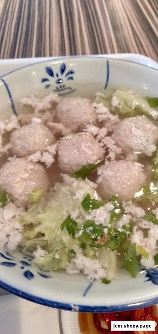 A close-up shot of a bowl of soup with meatballs, vegetables, and herbs.