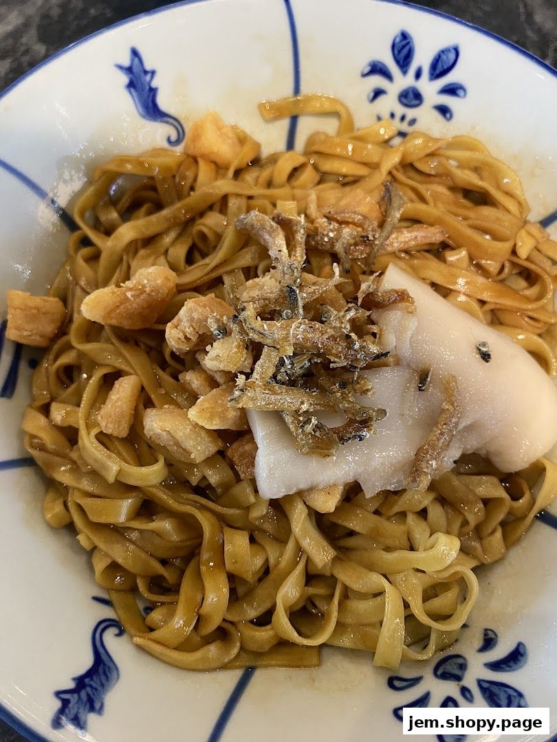 A close-up of a bowl of noodles with fish and crispy toppings.