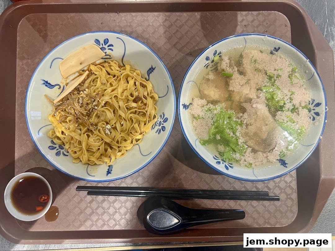 A tray with two bowls of noodles, one dry and one in soup, with a side of dipping sauce.