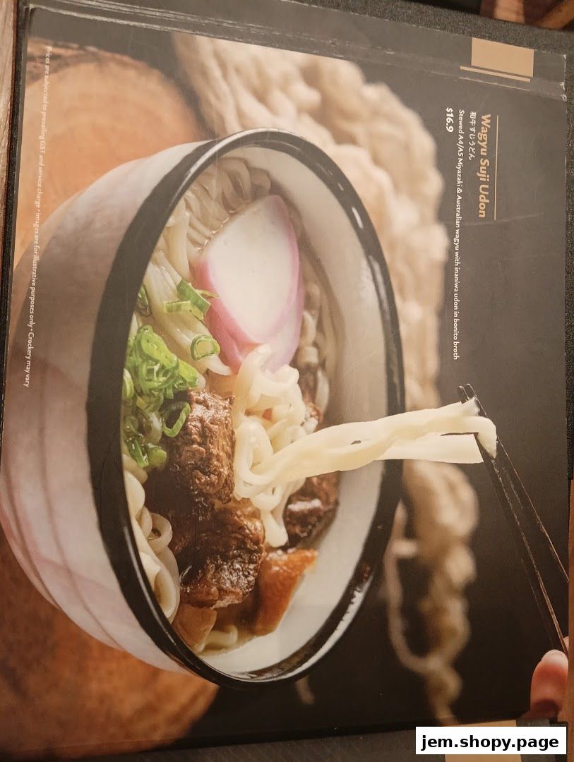 A close-up of a Wagyu Suji Udon dish with noodles being lifted by chopsticks.