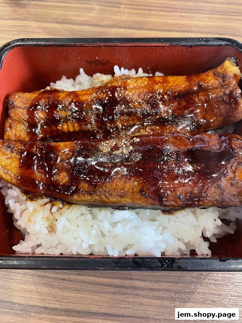 A close-up of grilled eel with teriyaki sauce served over white rice in a bento box.