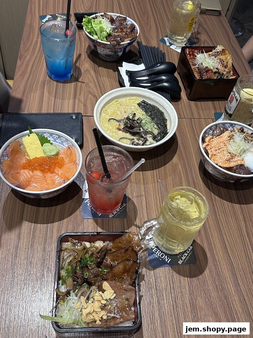 A table laden with various Japanese dishes and drinks, including ramen, donburi, and cocktails.