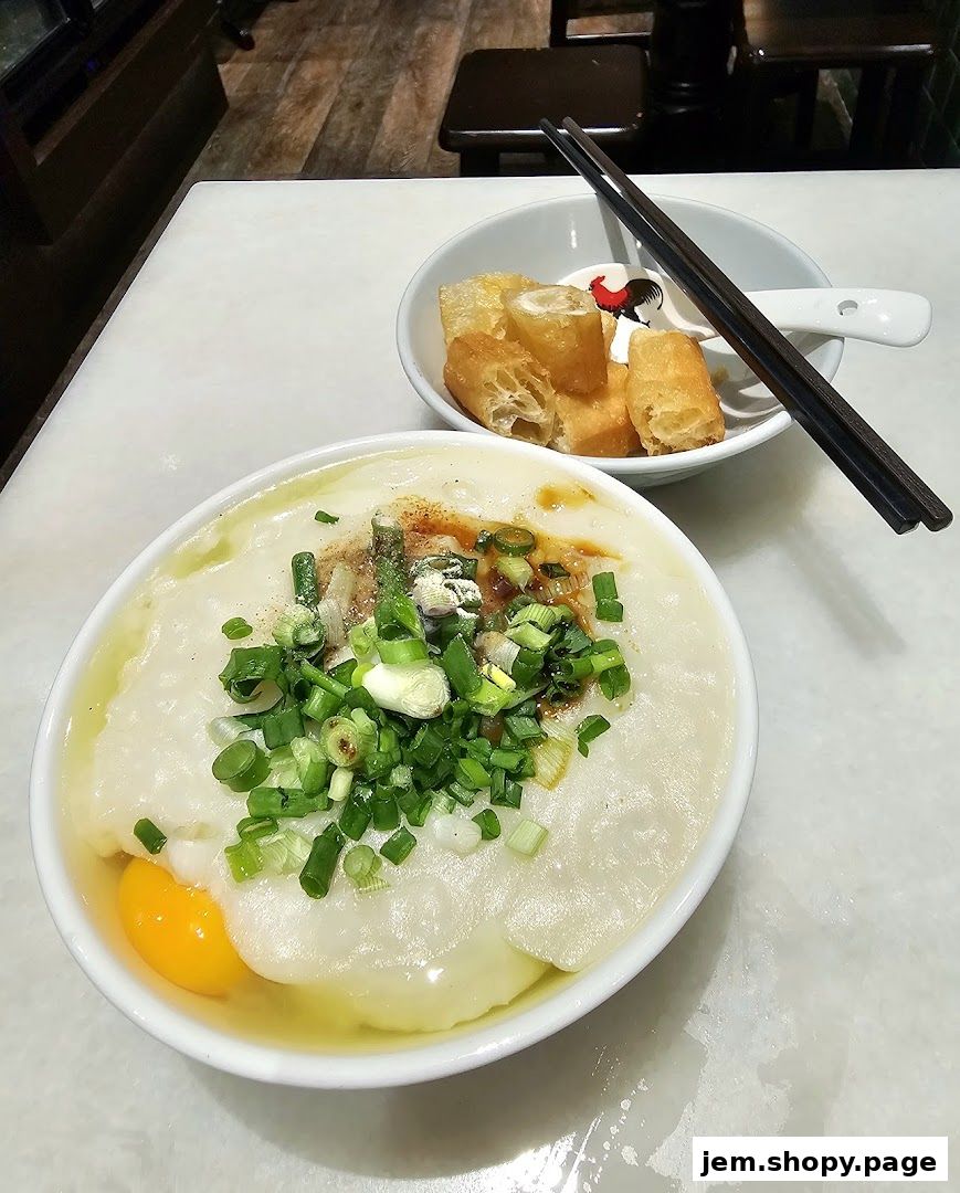 A bowl of traditional porridge with egg and scallions, served with fried dough sticks.