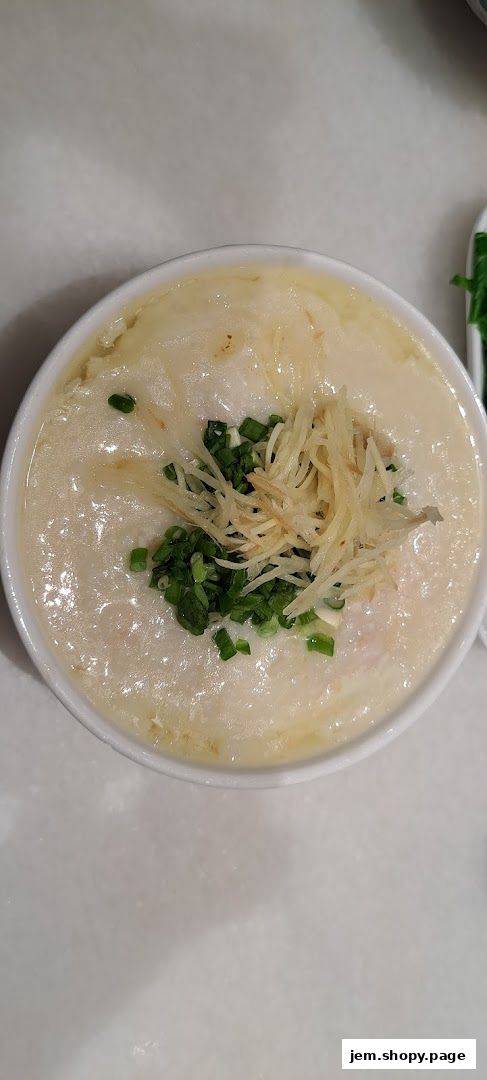 A close-up shot of a bowl of traditional porridge topped with scallions and ginger.