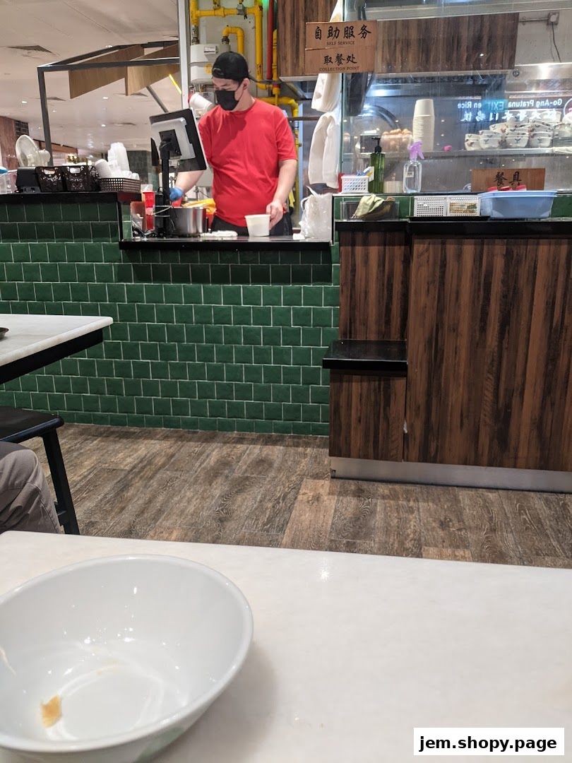 A staff member in a red shirt prepares food behind a counter at Ah Chiangs Traditional Porridge.