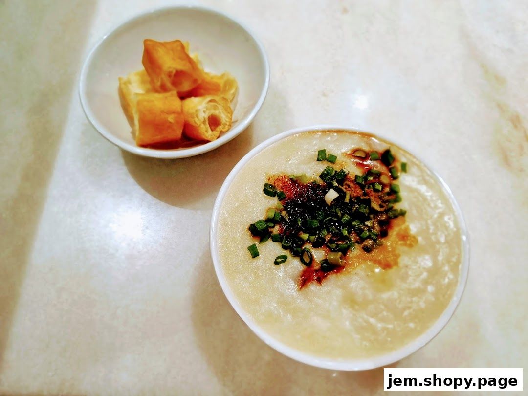 A bowl of traditional porridge topped with scallions and chili oil, served with fried dough sticks.