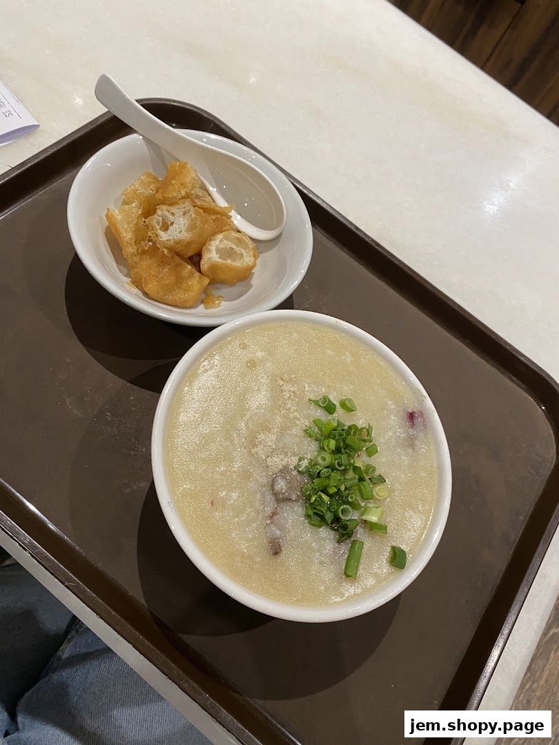 A bowl of traditional porridge with fried dough sticks and chopped scallions.