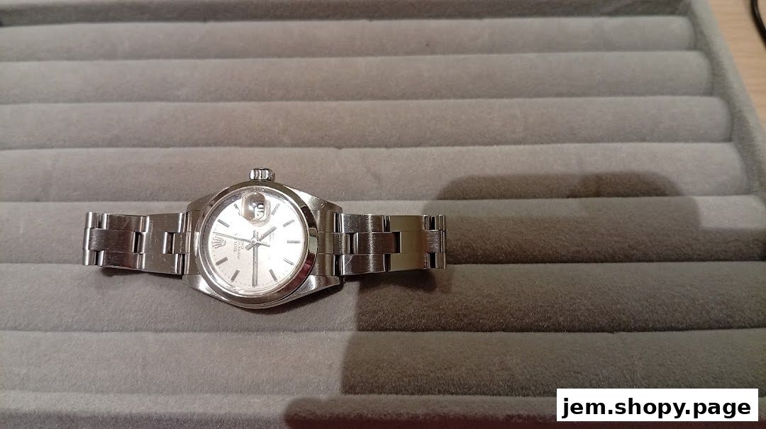 A close-up shot of a silver Rolex watch on a grey velvet display tray.