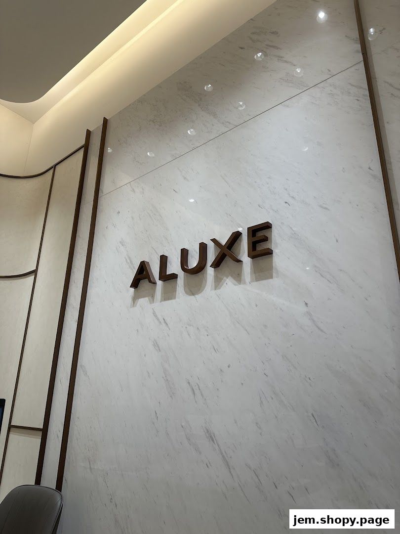 The ALUXE JEM logo is displayed on a marble wall with elegant lighting.