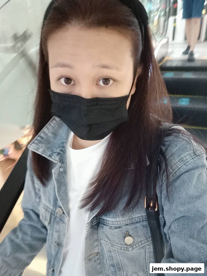 A woman wearing a denim jacket and a face mask on an escalator.