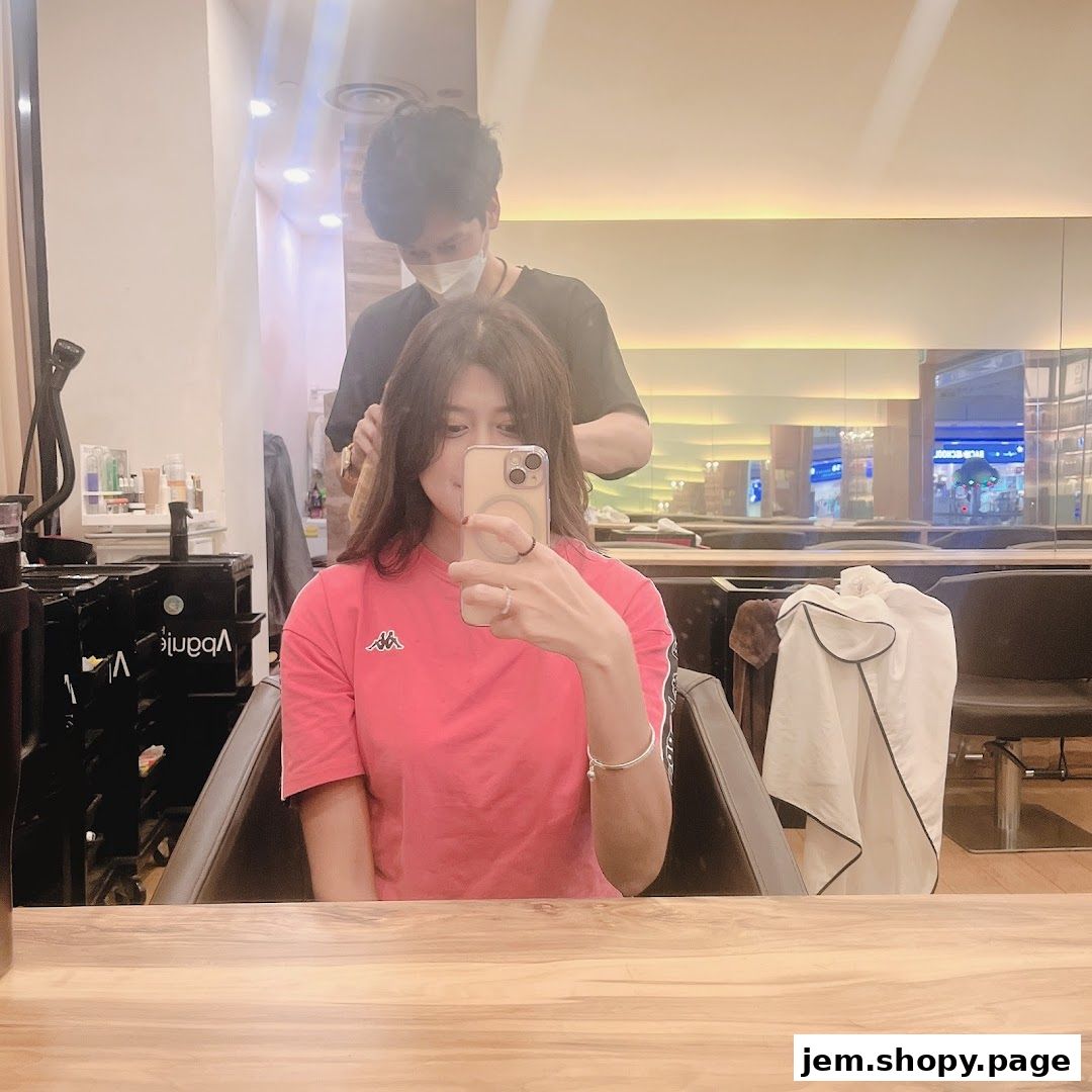 A woman takes a selfie while a stylist works on her hair in a salon.