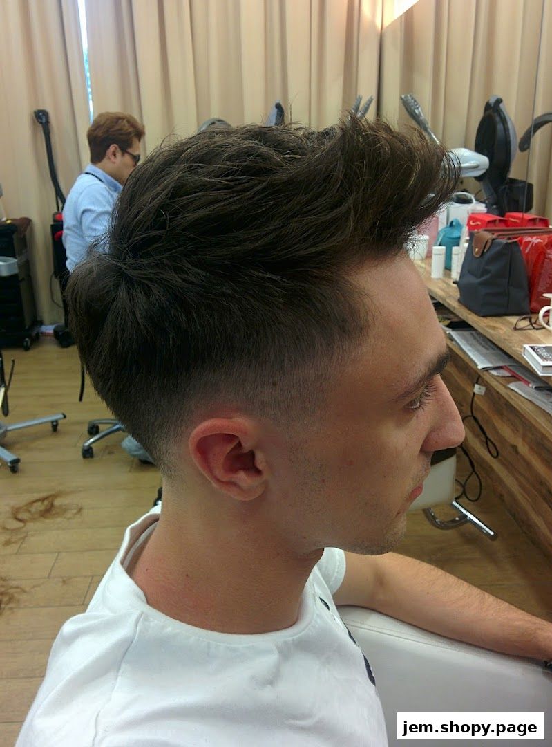 A man with a stylish fade haircut sits in a salon chair, with a stylist in the background.