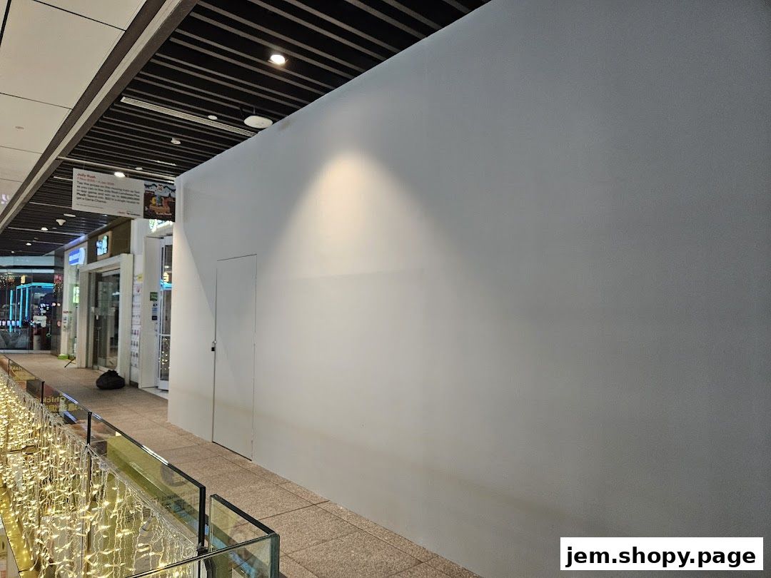 A blank white wall with a door and a sign on the left in a mall hallway.