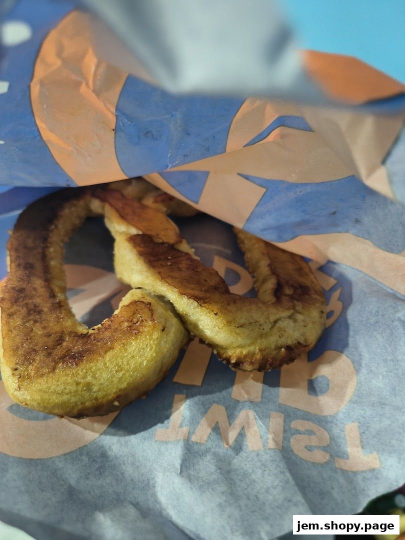 A close-up shot of a freshly baked pretzel peeking out of an Auntie Anne's paper bag.