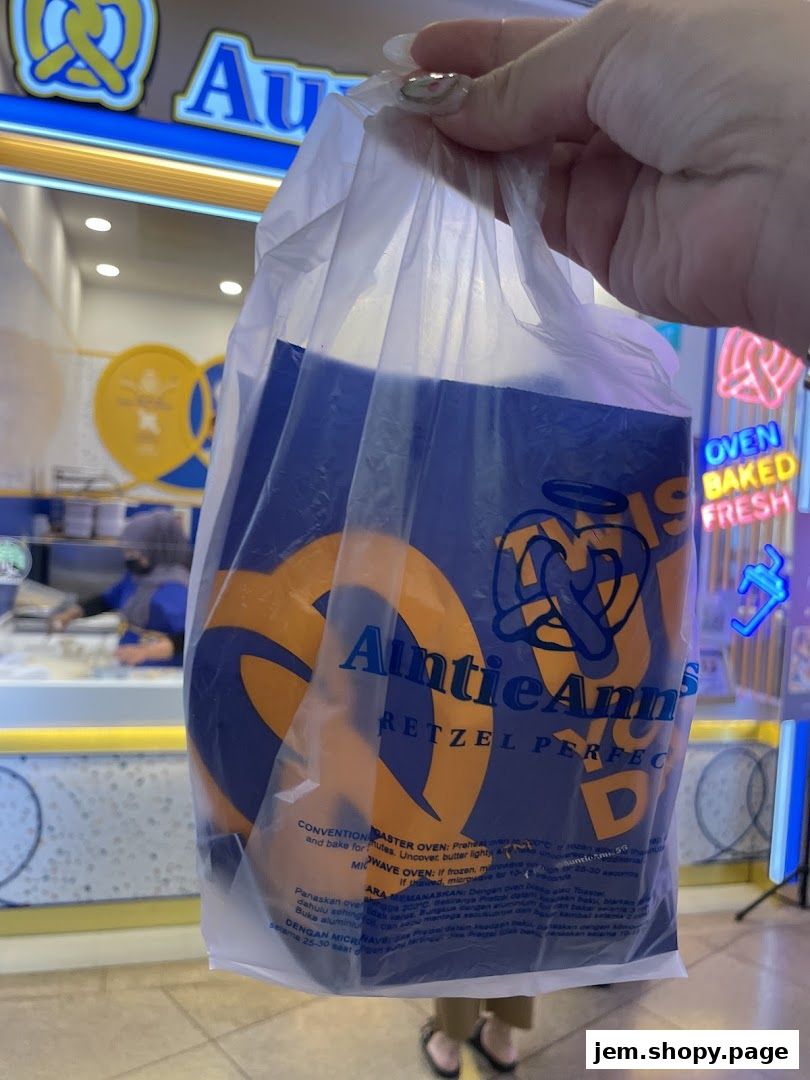 A person holds a plastic bag with Auntie Anne's pretzels in front of the shop.
