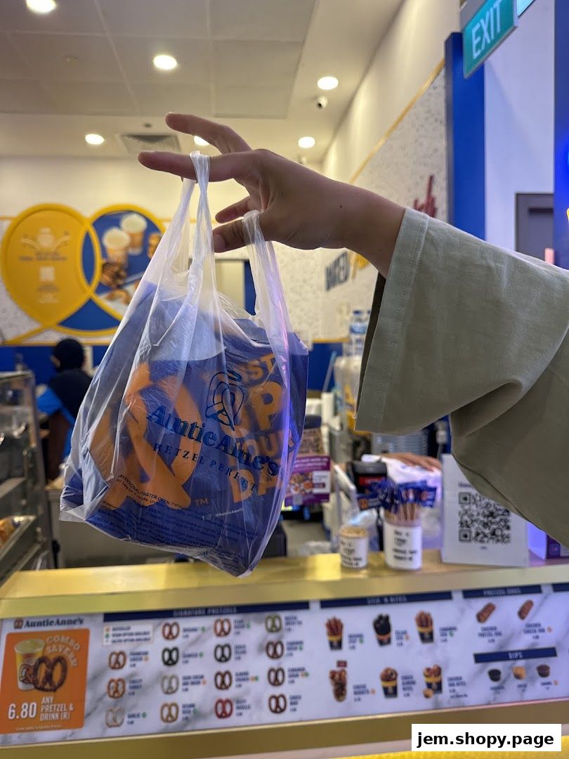 A hand holds a plastic bag filled with Auntie Anne's pretzels in front of the counter.