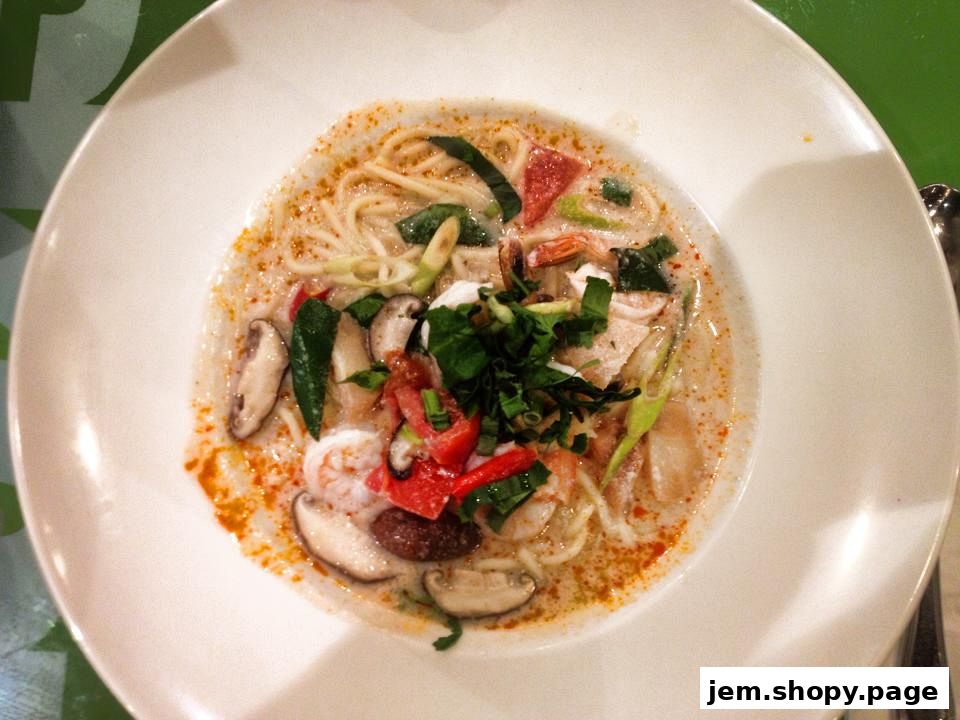 A close-up shot of a delicious bowl of Tom Yum soup with noodles, shrimp, mushrooms, and herbs.