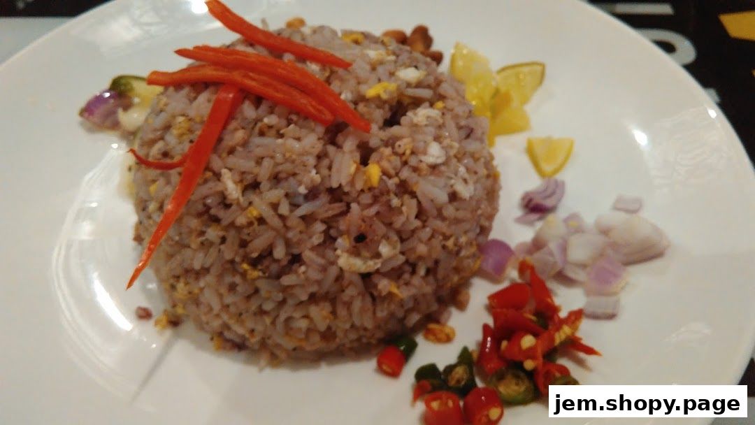 A plate of Thai fried rice garnished with chili, lemon, and onions.