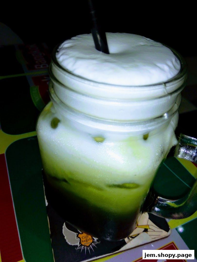 A refreshing green iced drink with a thick layer of foam in a glass jar.