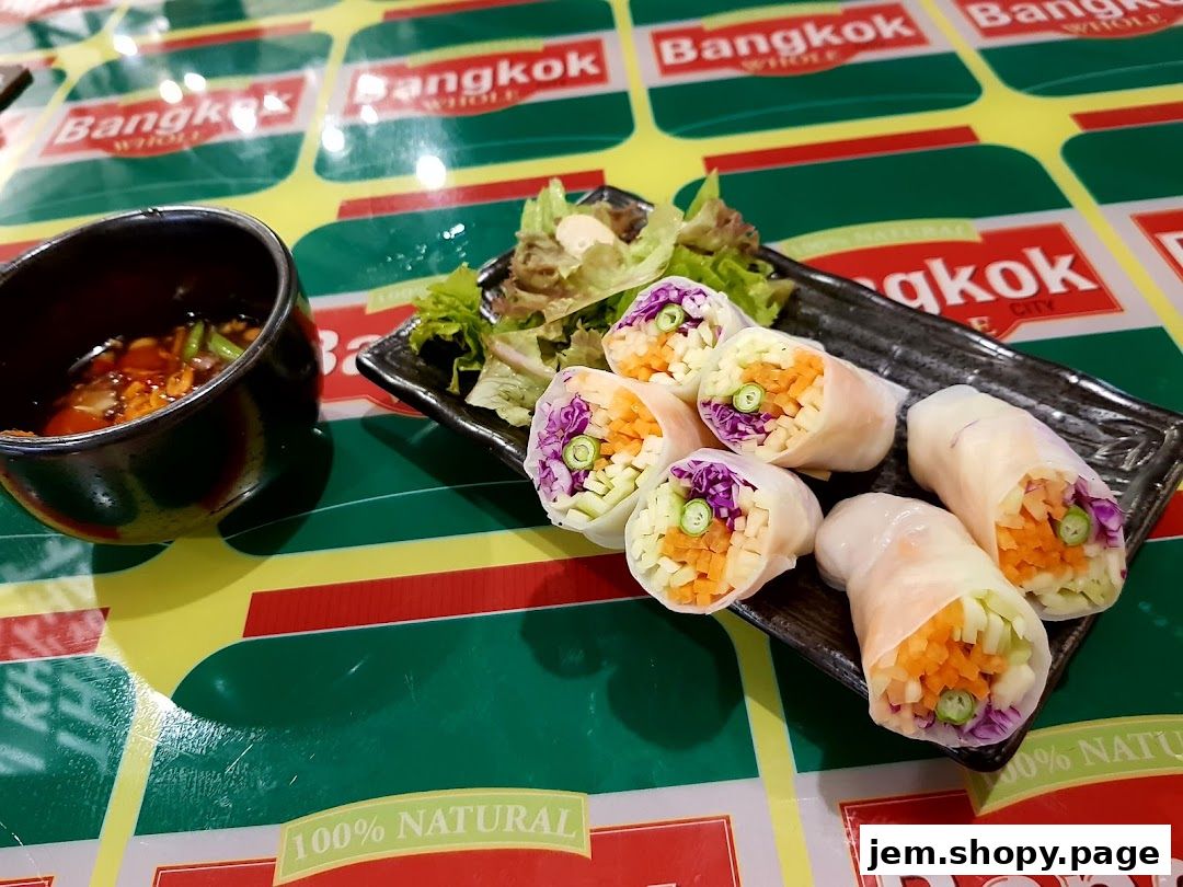 Fresh spring rolls with vegetables and a dipping sauce on a table with Bangkok branding.