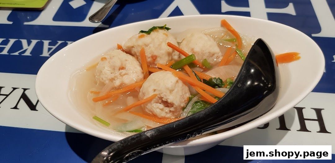 A bowl of Thai fish ball soup with carrots and greens, served with a black spoon.