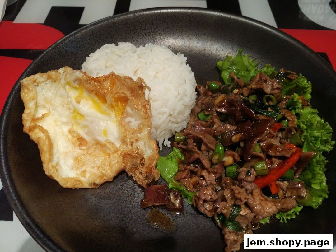 A plate of Thai food with rice, a fried egg, and stir-fried beef with vegetables.