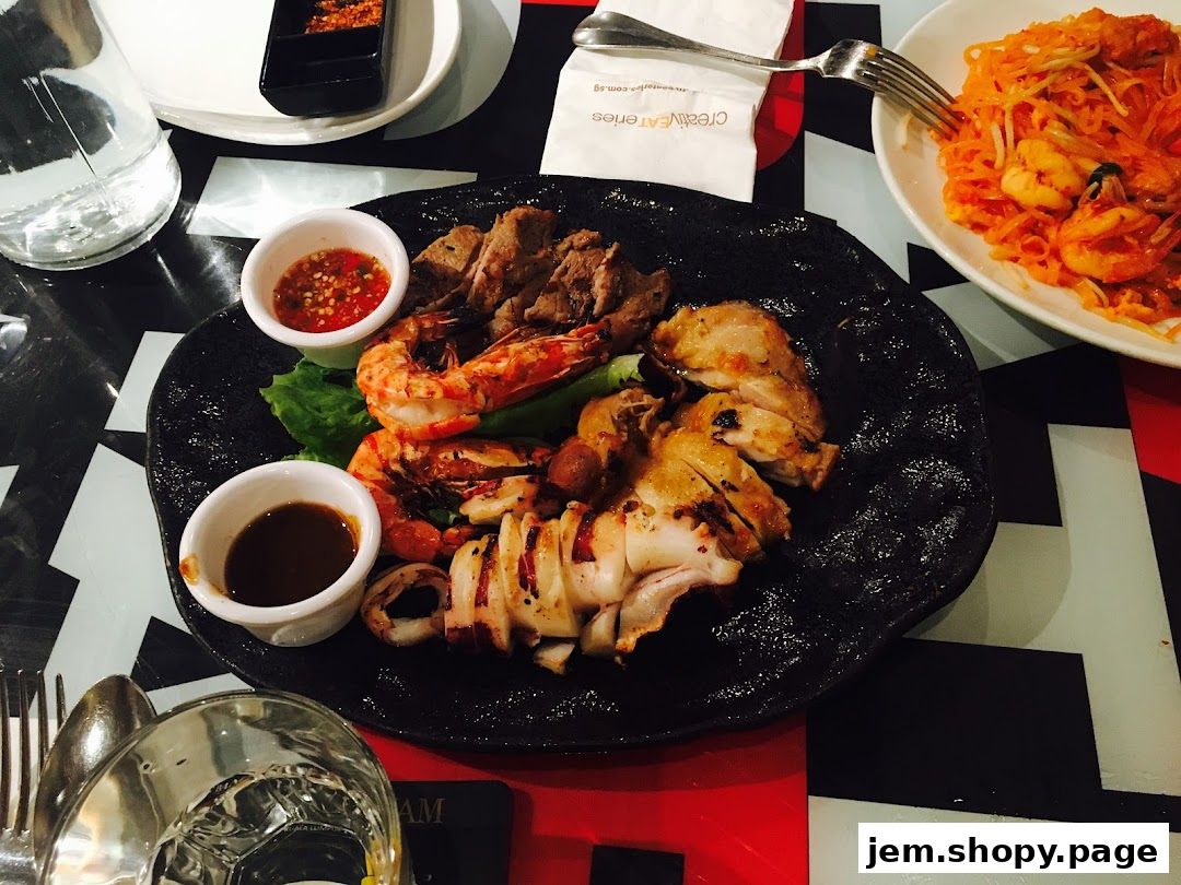 A platter of grilled meats, seafood, and a side of Pad Thai noodles.