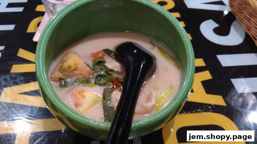A close-up of a bowl of creamy Thai soup with tomatoes and herbs.