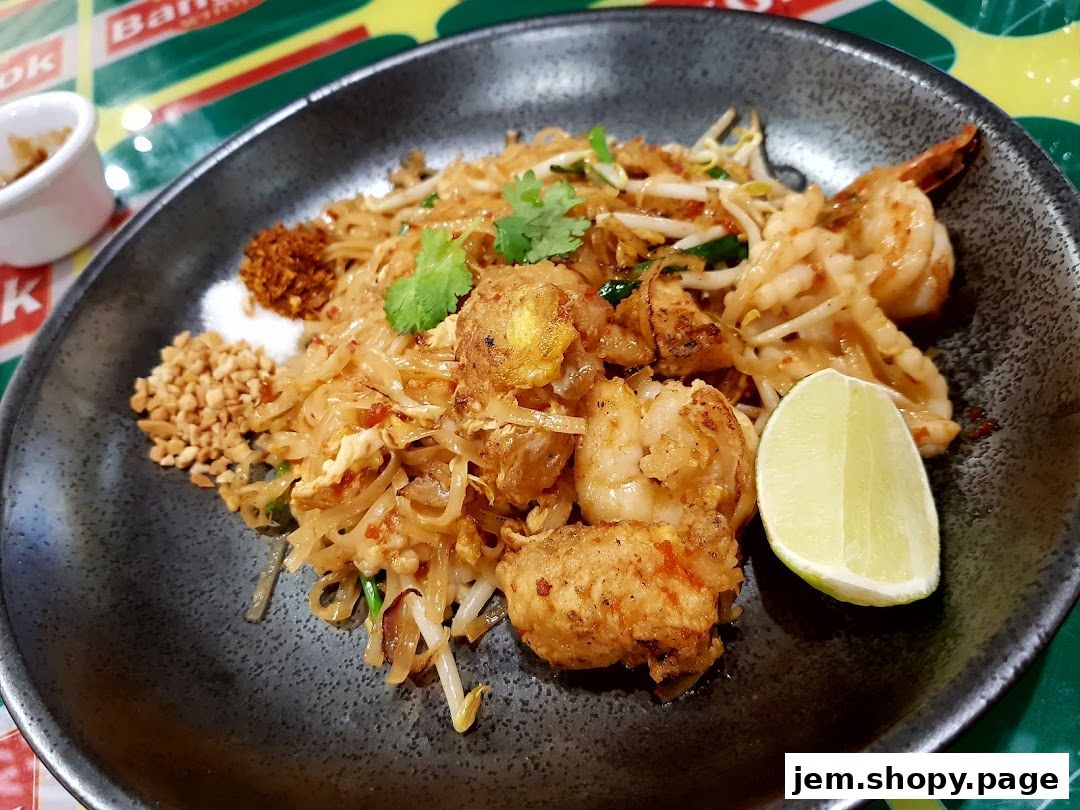A plate of Pad Thai with shrimp, peanuts, lime, and chili flakes.