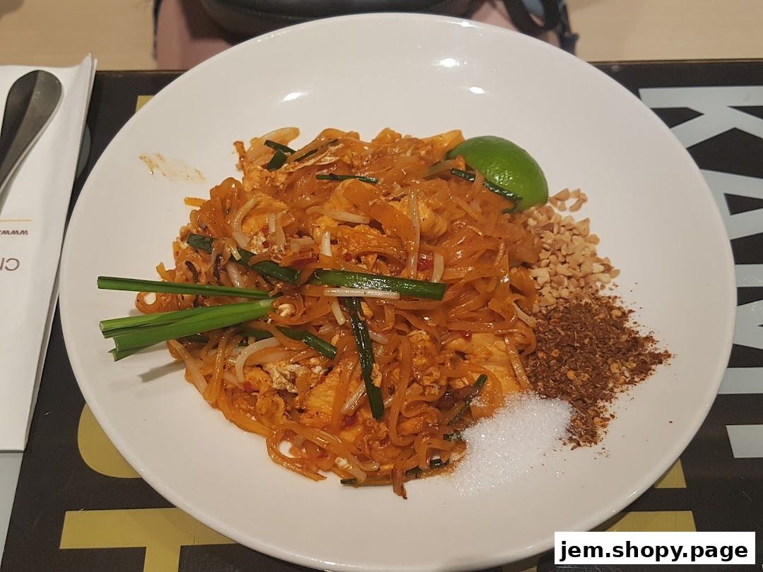 A plate of Pad Thai noodles with lime, peanuts, and chili flakes.