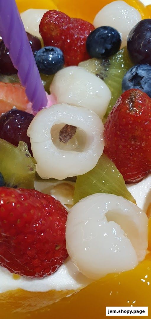 A close-up of a fruit cake topped with strawberries, blueberries, lychees, kiwi, and grapes.