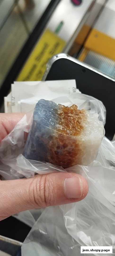 A hand holds a sweet treat wrapped in plastic, with a phone and receipts in the background.