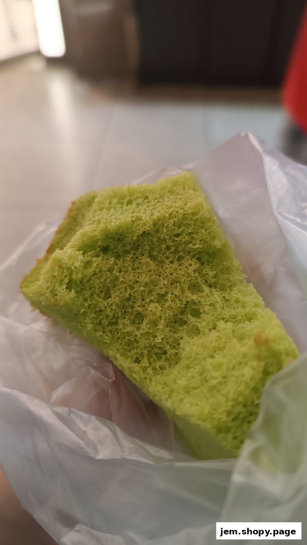 A close-up shot of a slice of bright green pandan cake in a plastic bag.