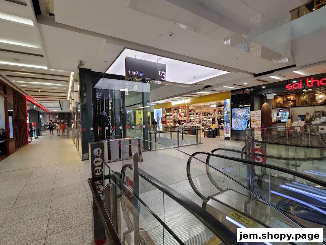 Interior view of a shopping mall with escalators, shops, and signage.