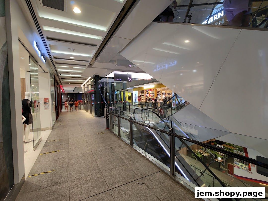 A modern shopping mall interior with escalators, shops, and a mannequin in a storefront.