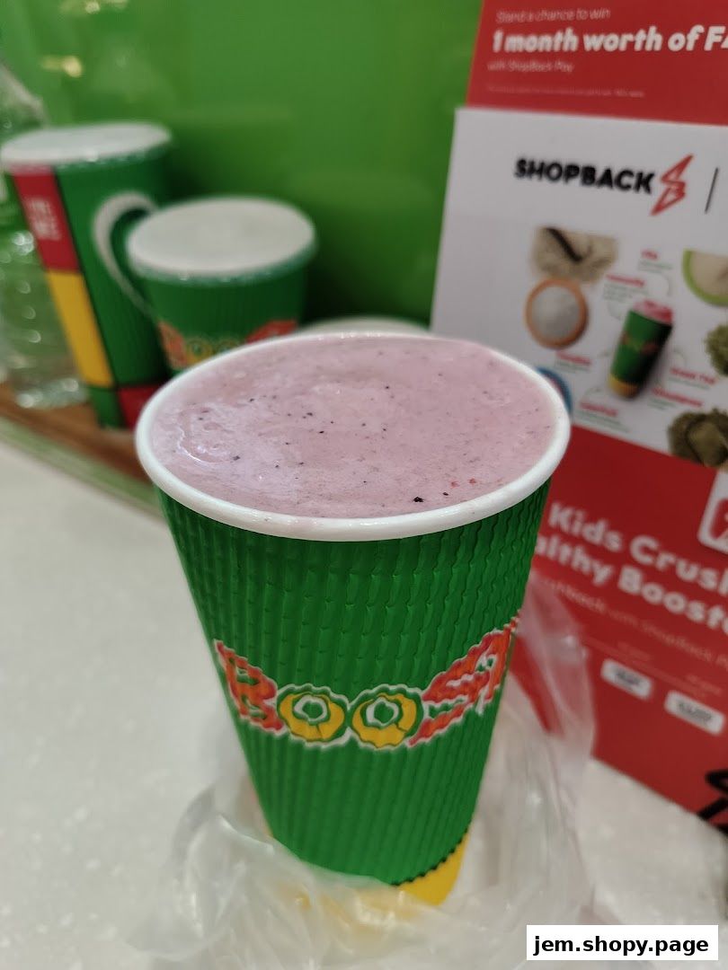 A close-up of a green Boost Juice cup filled with a pink smoothie, with other cups in the background.