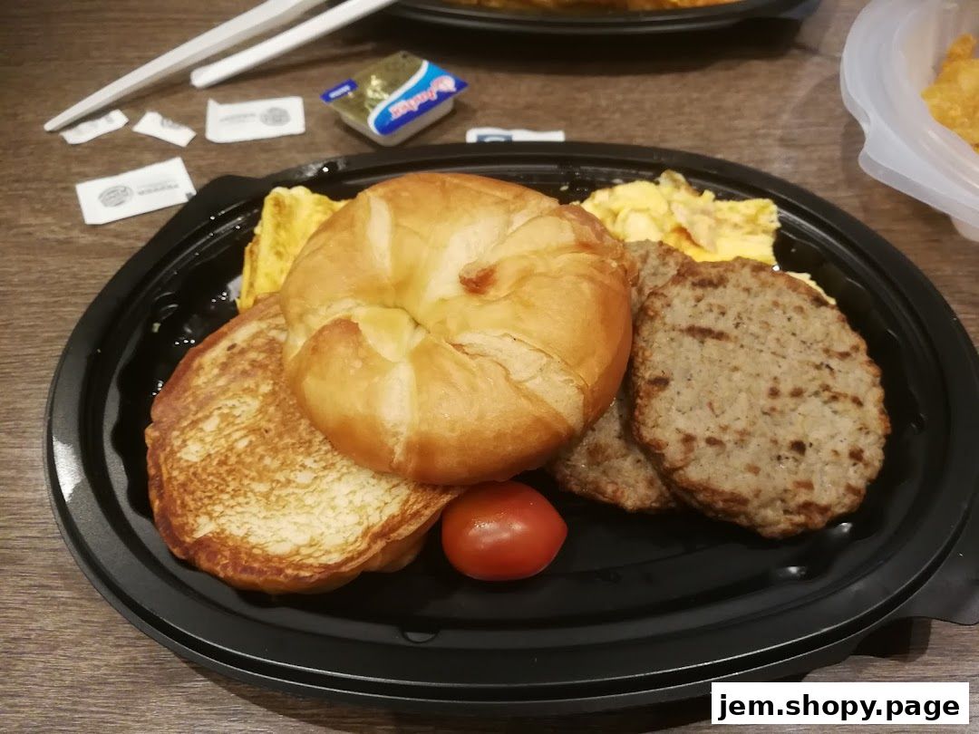 A delicious breakfast platter with a croissant, pancakes, sausage patties, scrambled eggs, and a cherry tomato.