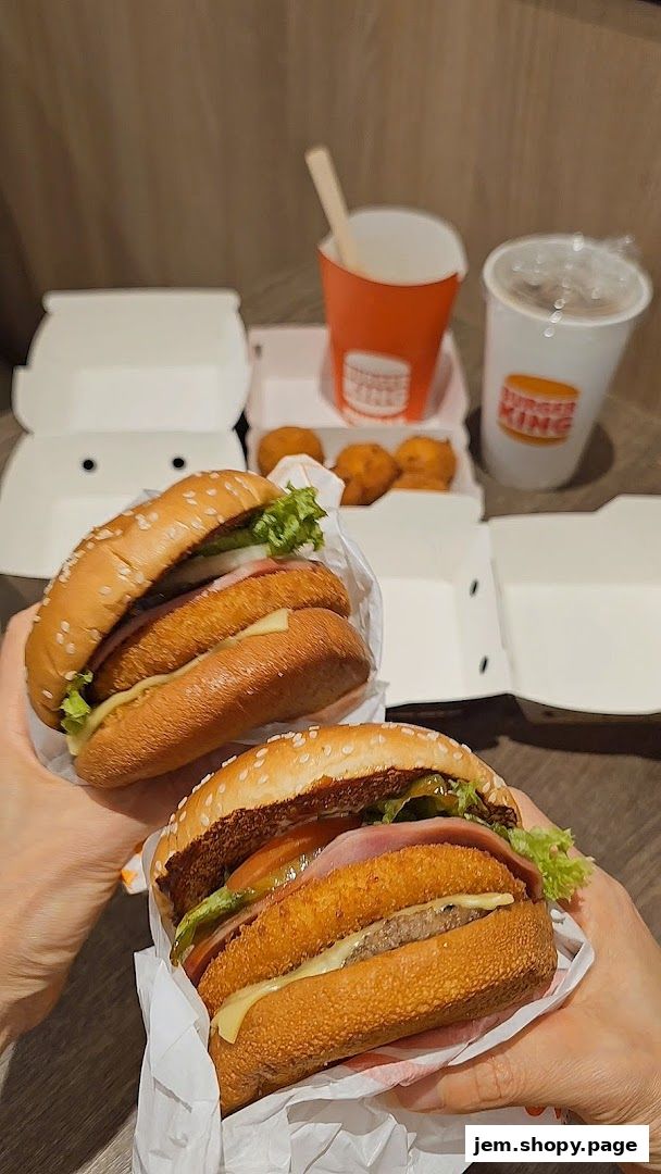 Two hands holding delicious Burger King burgers with sides and drinks.