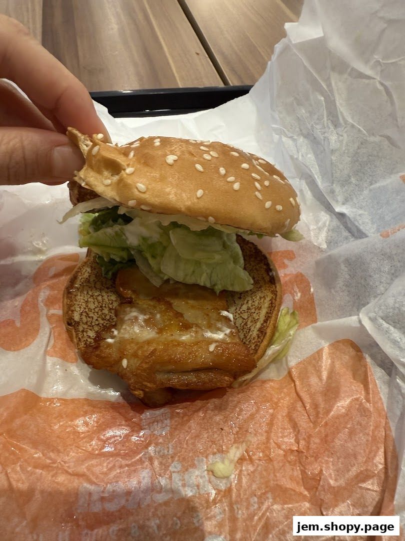 A hand holding a partially unwrapped Burger King burger with lettuce and sauce.