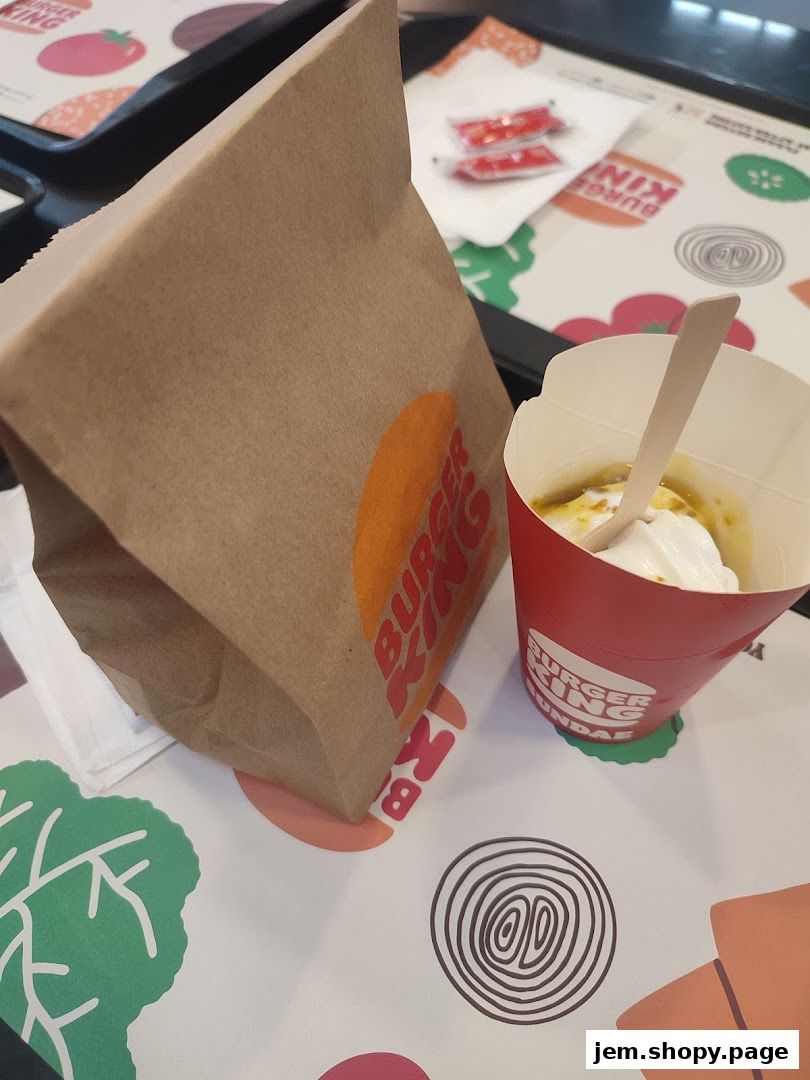 A Burger King paper bag and a sundae cup with a wooden spoon on a branded tray.