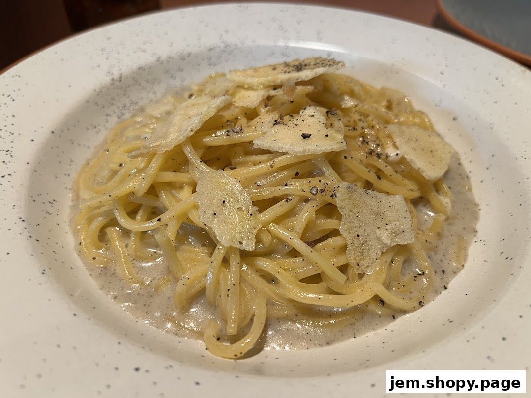 A close-up of a creamy pasta dish topped with cheese shavings and black pepper.