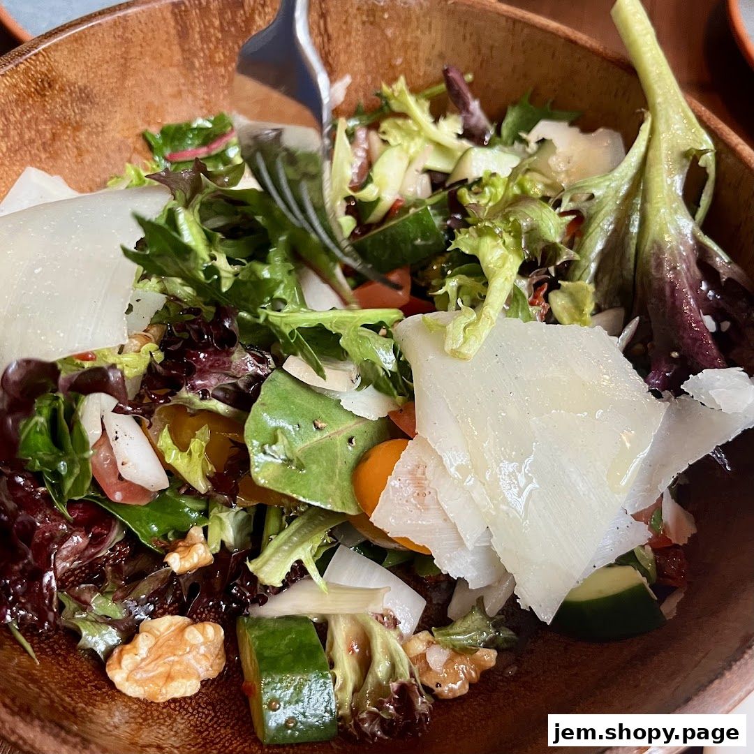 A close-up shot of a fresh salad with mixed greens, cheese shavings, and walnuts in a wooden bowl.